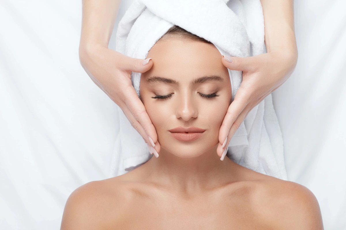 Woman receiving a professional facial treatment in Tulsa, OK, with a skincare therapist gently applying products to her face for skin cleansing and rejuvenation